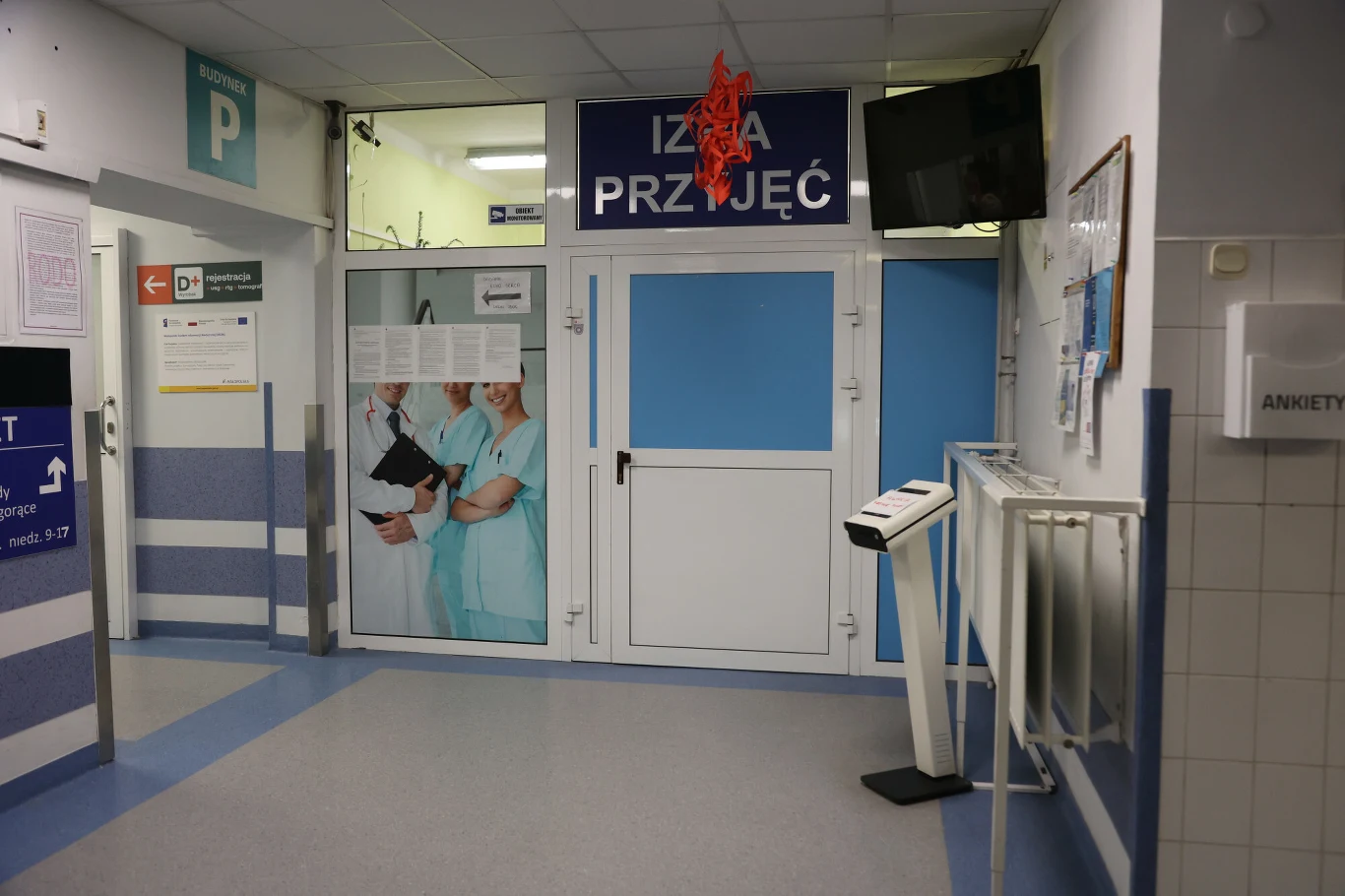 Do NFZ wpłynęło 36 wniosków dotyczących likwidacji lub przeprofilowania oddziałów szpitalnych Wejście do szpitalnej izby przyjęć z widocznym napisem, grafiką personelu medycznego i wagą lekarską.