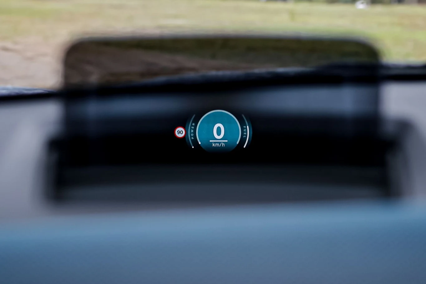 Wyświetlacz przezierny w samochodzie pokazujący aktualną prędkość 0 km/h oraz ograniczenie prędkości do 90 km/h.