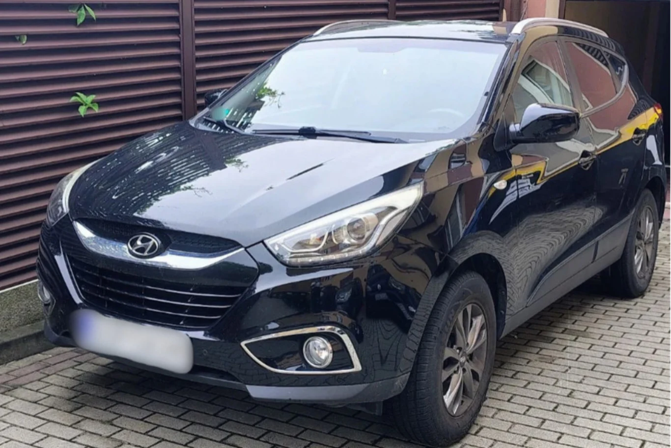 Czarny SUV marki Hyundai zaparkowany na brukowanej nawierzchni przy budynku z brązową elewacją.