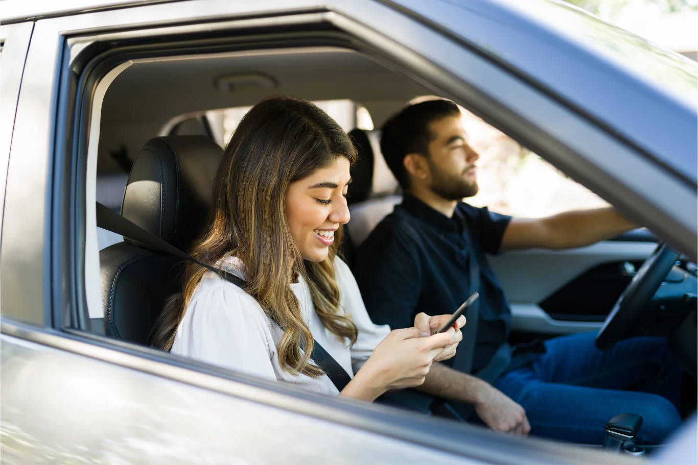 W walce z chorobą lokomocyjną może pomóc telefon. Kobieta na przednim siedzeniu samochodu korzysta z telefonu, podczas gdy mężczyzna prowadzi pojazd.
