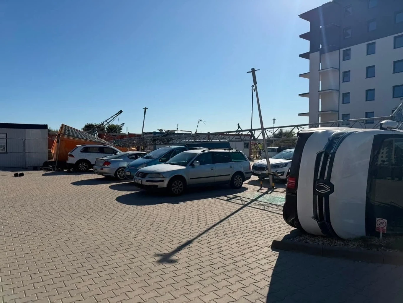 Wypadek żurawia budowlanego w Kaliszu Przewrócony dźwig leżący na zaparkowanych samochodach na parkingu przy budynku mieszkalnym.