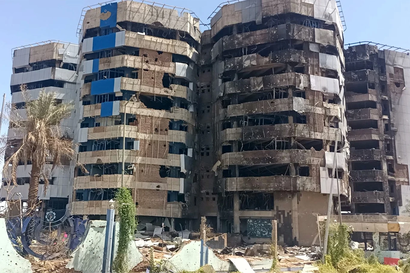 Zniszczony budynek banku centralnego Sudanu, 22 marca 2025 r. Wielopiętrowy budynek o czarnej, wypalonej elewacji z licznymi uszkodzonymi oknami i śladami pożaru, otoczony gruzem i zniszczonymi fragmentami infrastruktury miejskiej.