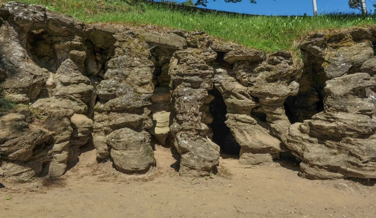 Grota Mechowska jest geologiczną osobliwością w Europie Północnej Formacje piaskowcowe Groty Mechowskiej z wąskim i niskim wejściem, otoczone ziemią i trawą.