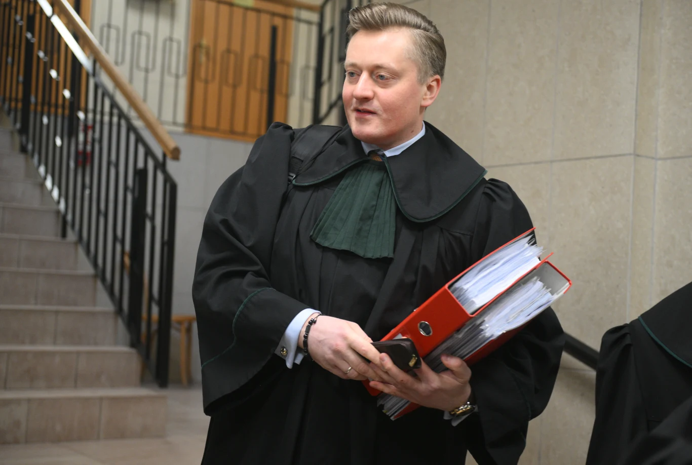 Mecenas Bartosz Lewandowski potwierdził złożenie przez Marcina Romanowskiego wniosku o list żelazny Bartosz Lewandowski w todze prawniczej z czerwonymi segregatorami dokumentów przy klatce schodowej sądu.