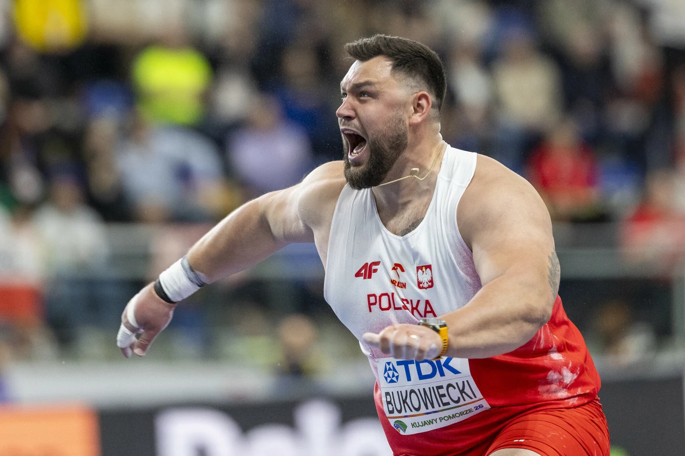 Konrad Bukowiecki Mężczyzna w stroju sportowym Polski wykrzykujący z uniesionymi ramionami, na torsie numer startowy z nazwiskiem Bukowiecki, dynamiczna scena z zawodów lekkoatletycznych.