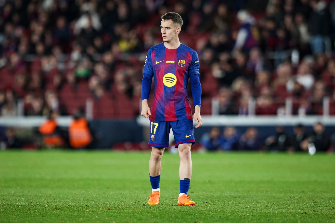 Piłkarz FC Barcelony w niebiesko-bordowym stroju z numerem 17 stoi na murawie stadionu podczas meczu, skoncentrowany na boiskowych wydarzeniach, w tle rozmyta publiczność.