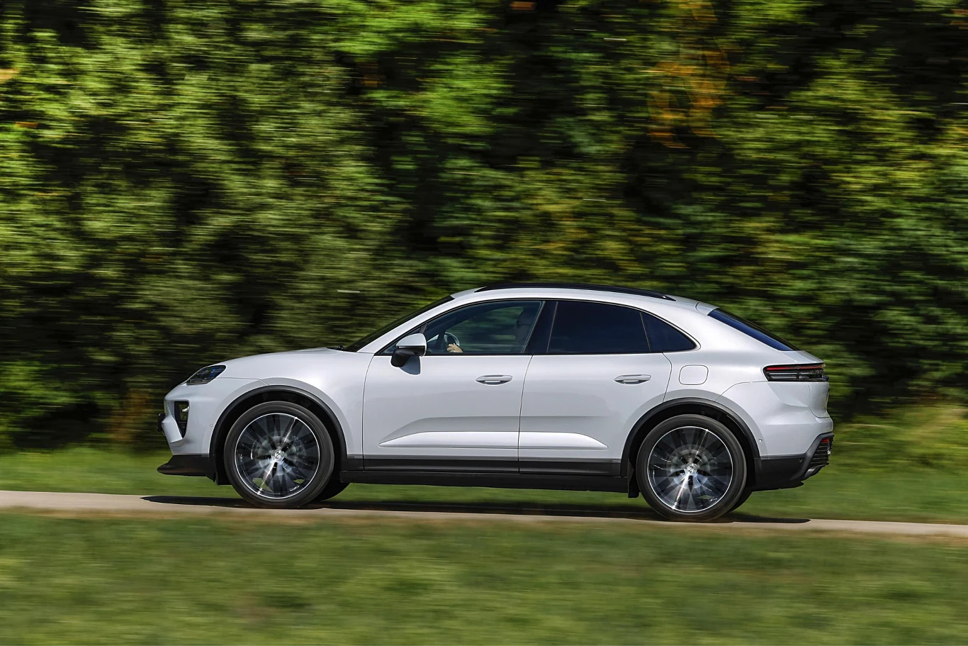 Białe, nowoczesne SUV coupe z przyciemnianymi szybami jedzie ścieżką wzdłuż zielonego lasu.