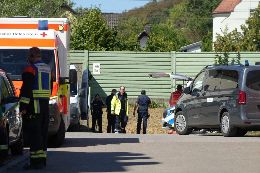 Siły specjalne policji federalnej prowadzą śledztwo w sprawie podejrzanego ładunk na terenie dworca kolejowego w Treuchtlingen Policja i ratownicy przy dworcu w Treuchtlingen, karetka i radiowozy na poboczu, w tle budynki i zielony płot.