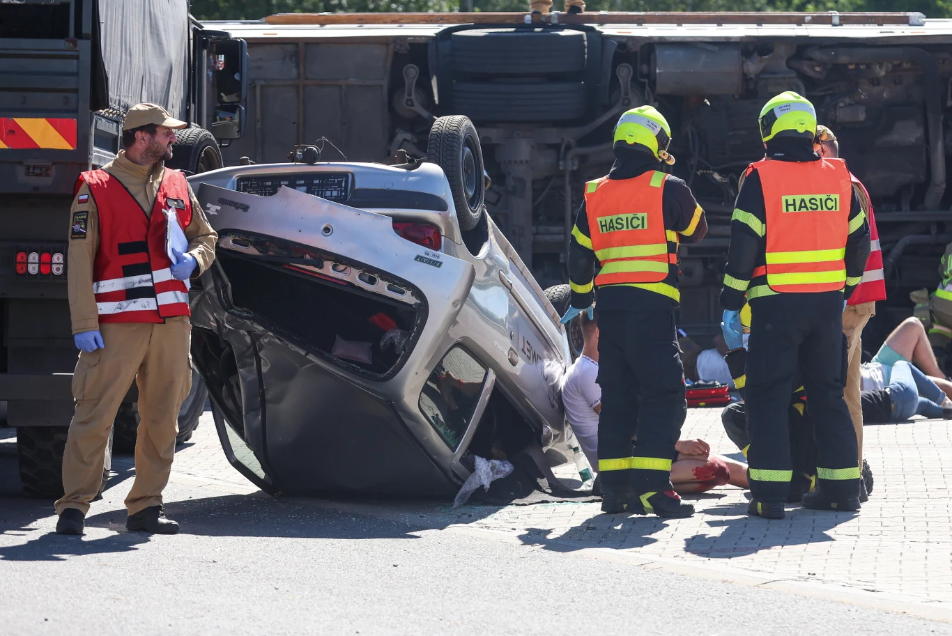 Taran na autostradzie A1 Strażacy udzielają pomocy przy przewróconym na dach samochodzie, obok leży wywrócona ciężarówka, a wokół znajdują się poszkodowani wymagający interwencji ratowników.