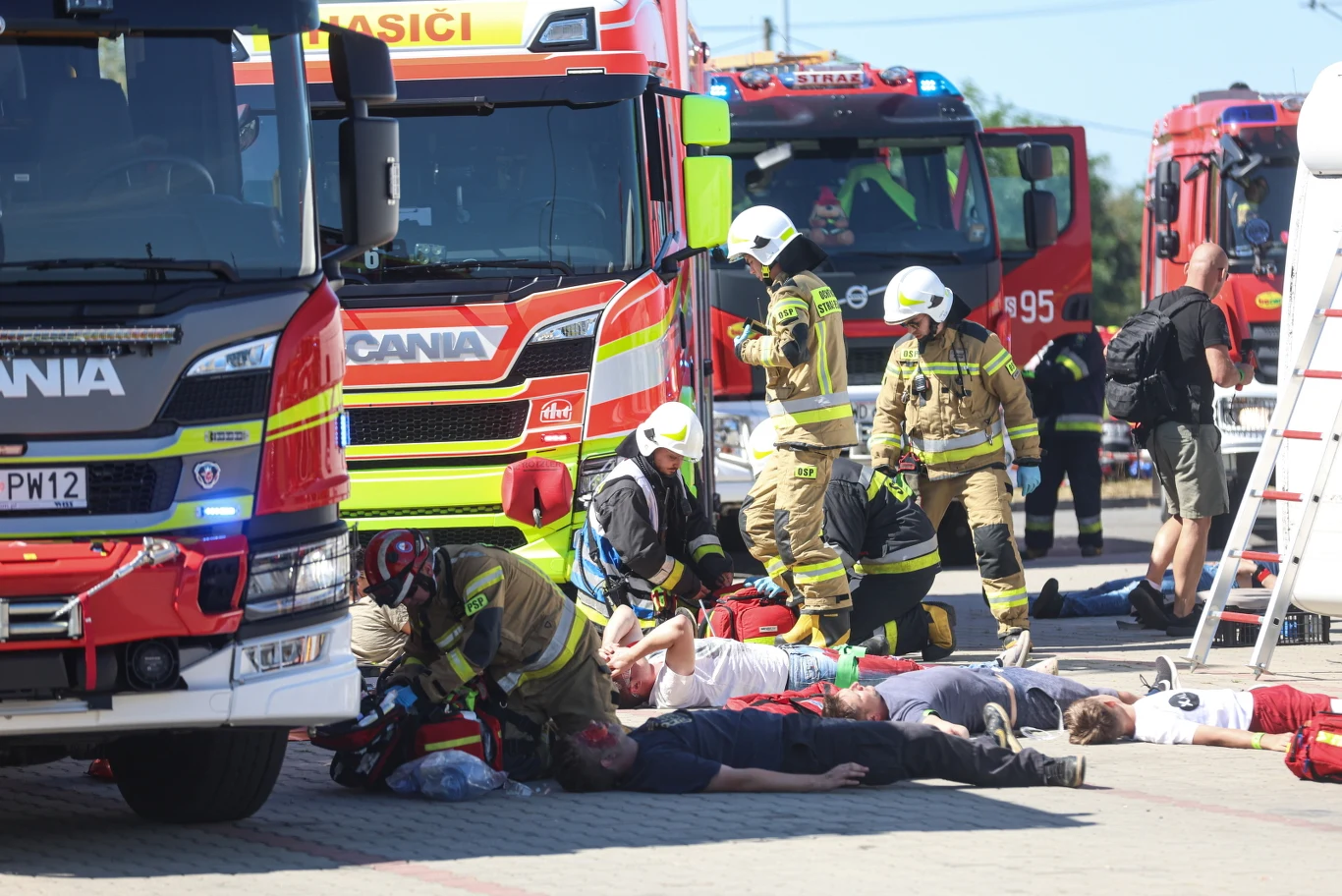 Taran na autostradzie A1 Strażacy udzielający pomocy kilku poszkodowanym osobom leżącym na ziemi obok wozów strażackich podczas akcji ratunkowej.
