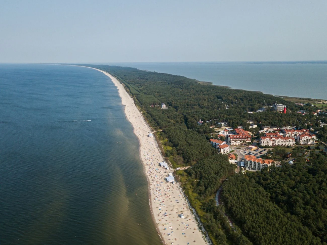 Wielbłądzi Garb ma status najwyższej stałej wydmy w Europie Wielbłądzi Garb, najwyższa stała wydma Europy; piaszczysta plaża przy brzegu morza, las i zabudowania w tle.