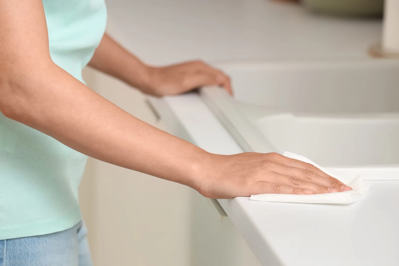 Włosi stosują pewny trik na ładnie pachnący dom od pokoleń. Osoba czyści biały blat kuchenny jasną ściereczką przy zlewie, nawiązując do dbania o domową czystość.