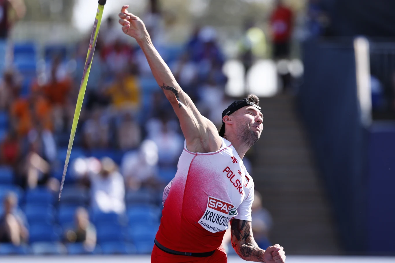 Marcin Krukowski Lekkoatleta w stroju reprezentacji Polski dynamicznie rzuca oszczepem na stadionie sportowym, koncentrując się na wykonaniu technicznego ruchu podczas zawodów.