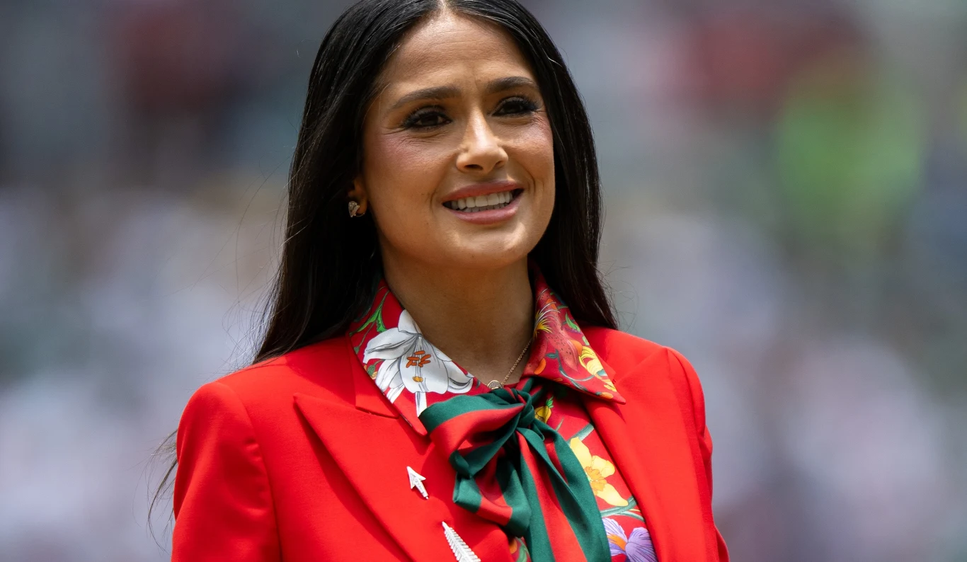 Salma Hayek Salma Hayek w czerwonej marynarce i koszuli w kwiatowy wzór z zieloną kokardą pod szyją.