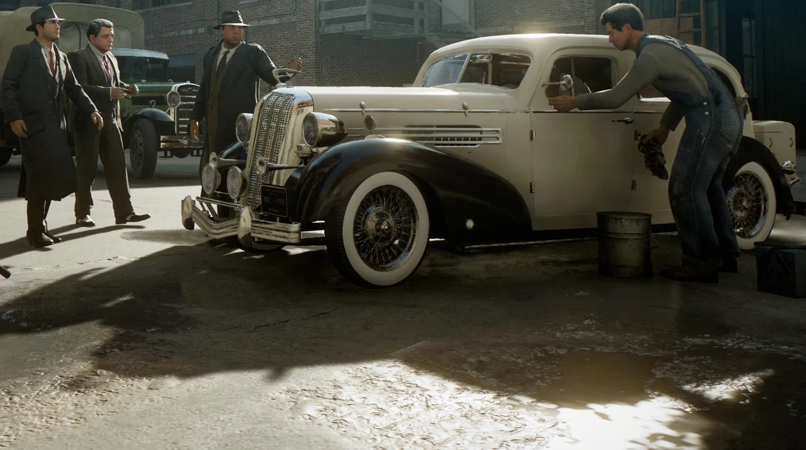 Mafia Definitive Edition Czterech mężczyzn w garniturach i płaszczach stoi przy klasycznym aucie, mechanik czyści przednie koło.