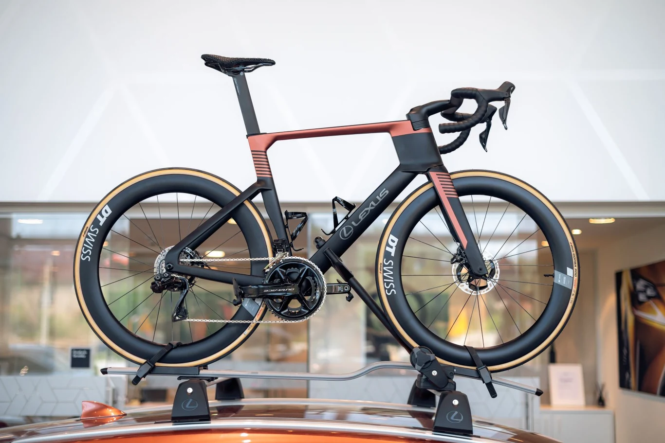 Lexus Race Bike waży zaledwie 8 kg. Nowoczesny rower szosowy w czarno-miedzianych kolorach zamocowany na bagażniku dachowym samochodu, wyróżniający się aerodynamiczną ramą i wysokimi, karbonowymi kołami DT Swiss.
