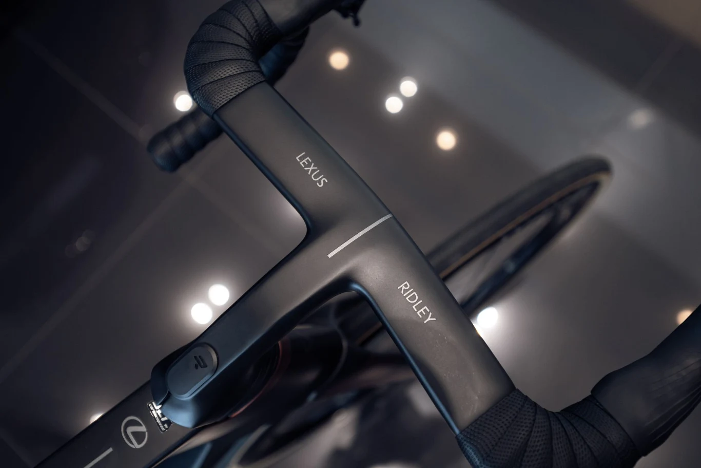 Ceny Lexusa Race Bike zaczynają się od 10 500 euro. kierownica roweru szosowego z napisami Lexus i Ridley, owinięta czarną taśmą, widoczny błyszczący fragment ramy oraz częściowo koło przednie