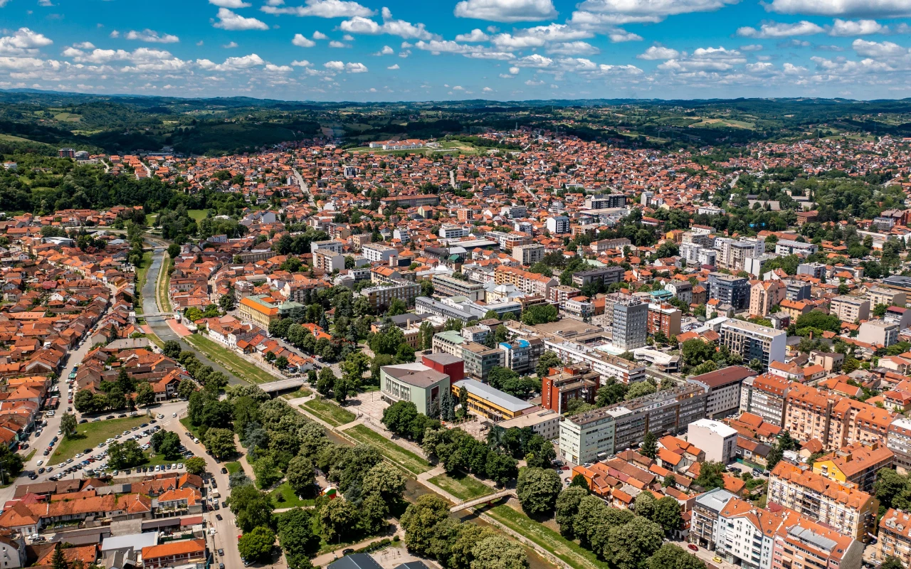 Valjevo Rozległa panorama Valjeva, z gęstą zabudową i licznymi ulicami otoczonymi zielenią, rozciągająca się po horyzont.