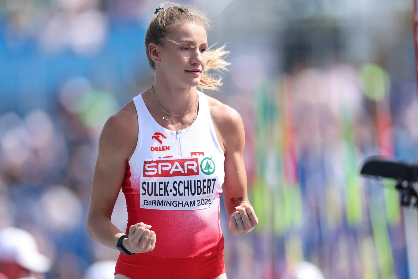 Adrianna Sułek-Schubert Lekkoatletka w biało-czerwonym stroju z nazwiskiem Sulek-Schubert oraz napisem Birmingham 2026 na numerze startowym, z zaciśniętymi pięściami, wyrażająca emocje na stadionie sportowym.