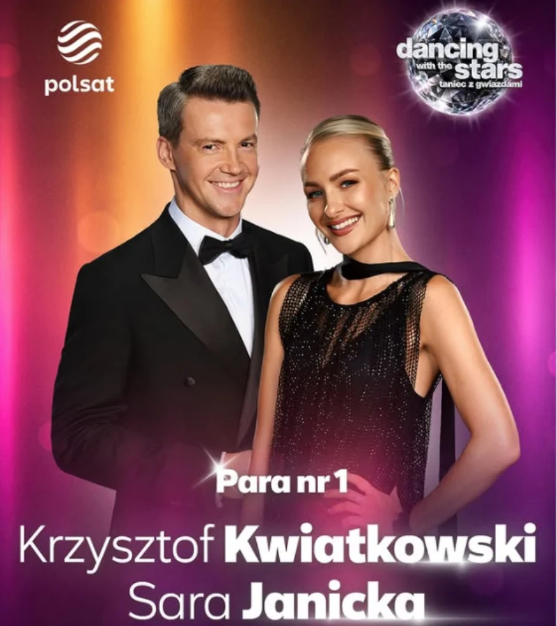 Krzysztof Kwiatkowski i Sara Janicka w eleganckich, wieczorowych strojach, stoją obok siebie uśmiechnięci, na kolorowym tle z logo programu 'Dancing with the Stars. Taniec z Gwiazdami' oraz oznaczeniem pary numer 1.