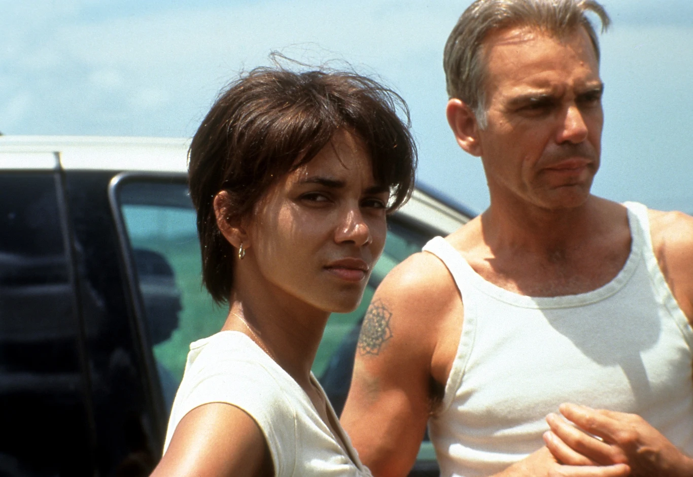 Halle Berry i Billy Bob Thornton w filmie "Czekając na wyrok" Dwie osoby stoją obok siebie na zewnątrz w słoneczny dzień, kobieta patrzy w stronę aparatu, mężczyzna w białym podkoszulku ma poważny wyraz twarzy.