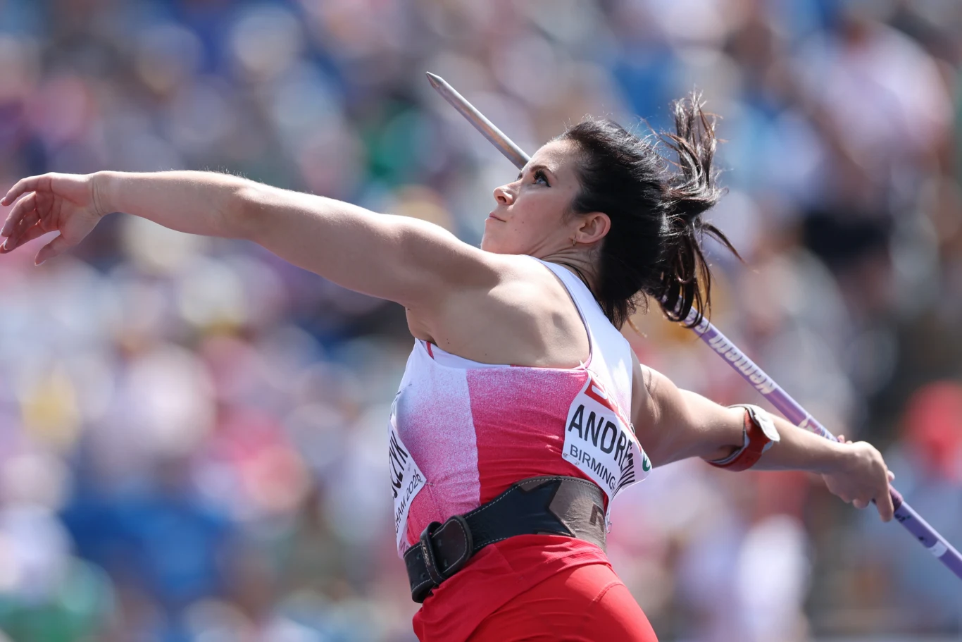 Zawodniczka w sportowym stroju dynamicznie wyrzuca oszczep podczas zawodów lekkoatletycznych, koncentrując się na wykonaniu technicznego rzutu.