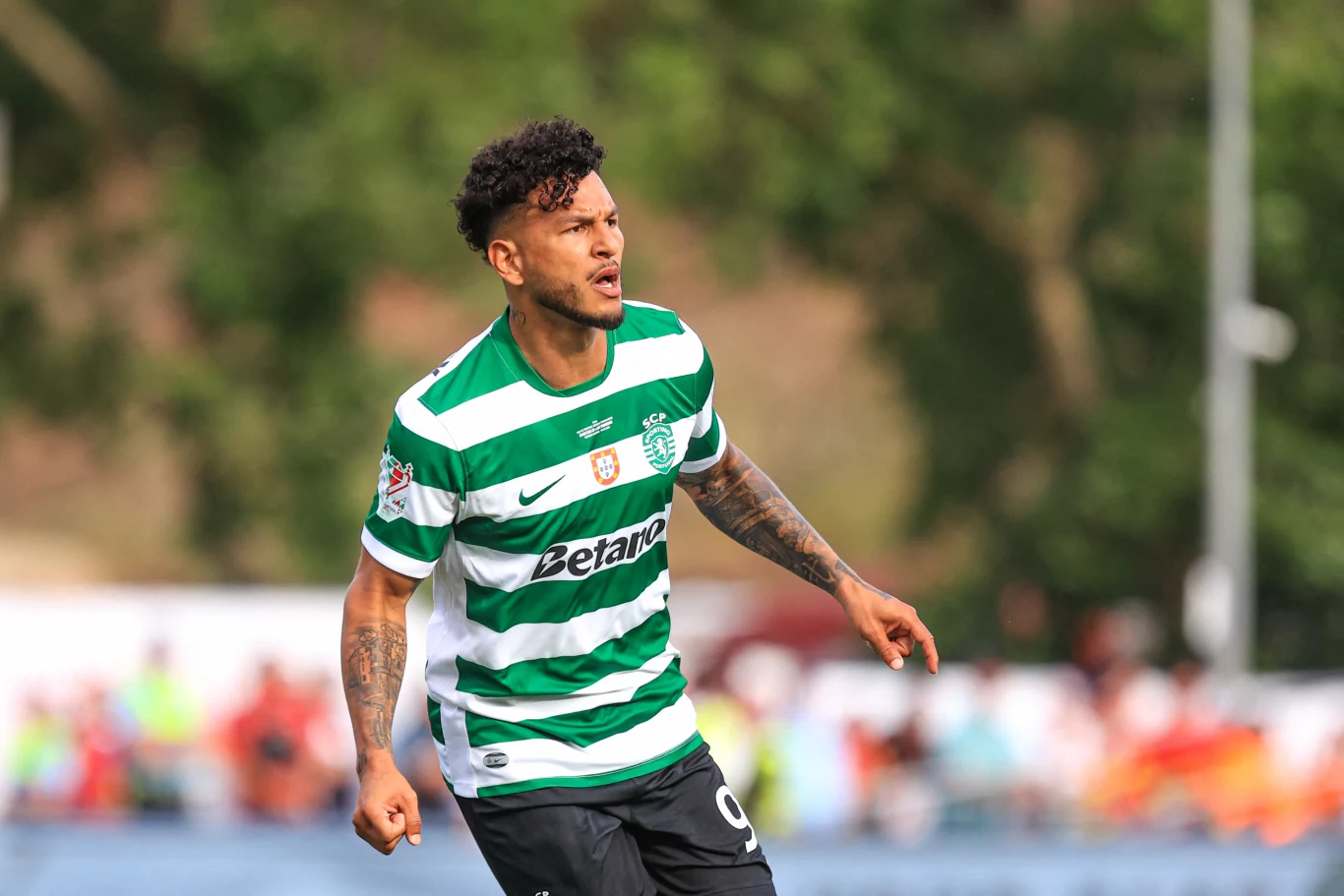 Piłkarz w zielono-białej koszulce z logo Sporting CP biegnie po murawie podczas meczu, skupiony i gotowy do podjęcia akcji.