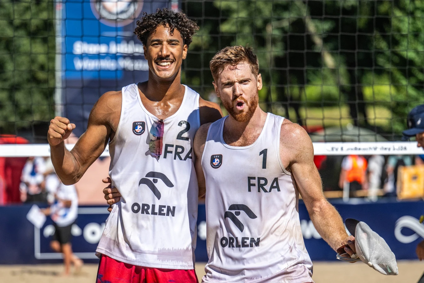 Francuzi mają swoich przedstawicieli w ćwierćfinale mistrzostw Europy Dwóch siatkarzy plażowych w biało-niebieskich strojach reprezentacji Francji, stojących przy siatce na piaszczystym boisku, wyraża radość po zakończonym meczu.