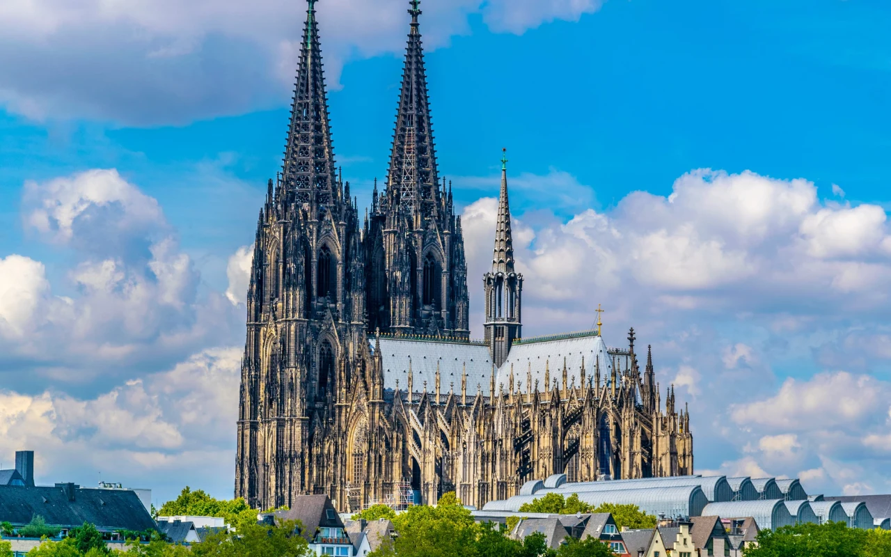Katedra Kolońska Panorama zdominowana przez Katedrę Kolońską, z dwiema wysokimi wieżami, pod błękitnym niebem z białymi chmurami.