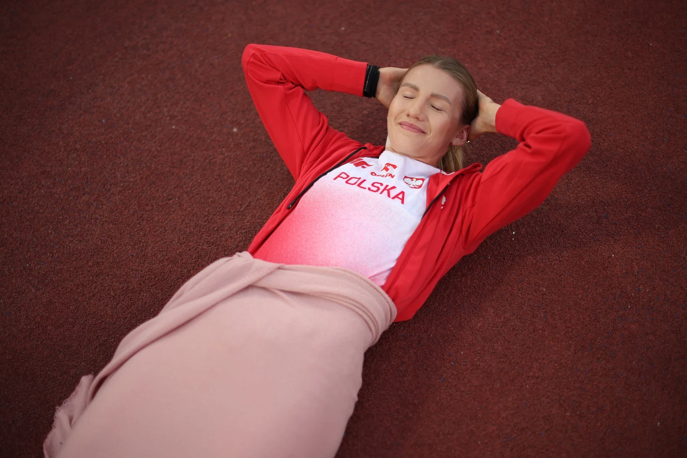 Adrianna Sułek-Schubert, Birmingham 2026 Sportsmenka w stroju reprezentacji Polski leżąca na bieżni z rękami pod głową i przykryta kocem po biodra, zrelaksowana i uśmiechnięta.
