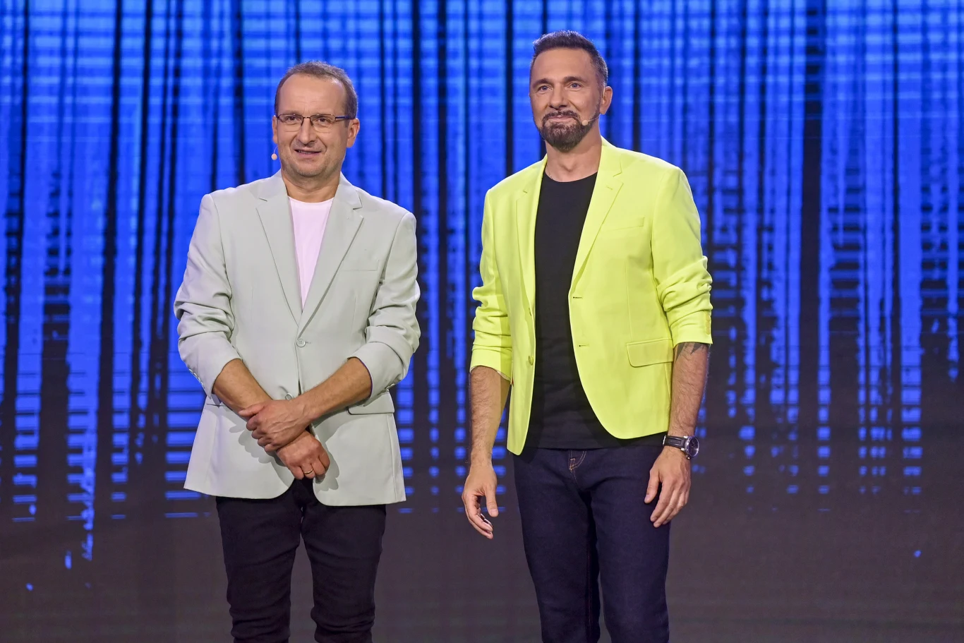 Robert Górski i Robert Korólczyk Robert Górski i Robert Korólczyk w jasnych marynarkach na tle niebieskiej, abstrakcyjnej scenografii.