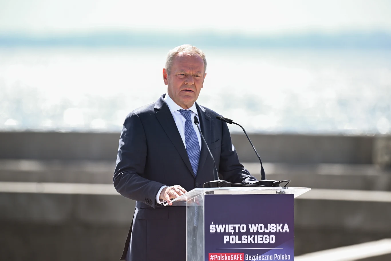 Premier Donald Tusk podczas uroczystości w Gdyni Premier Donald Tusk w garniturze przemawia przy mównicy 'Święto Wojska Polskiego' nad morzem w Gdyni.