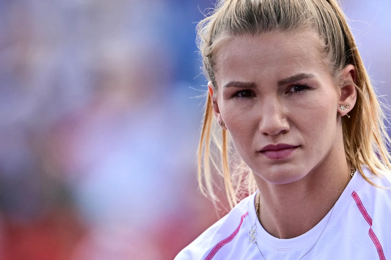 Kobieta o blond włosach spiętych w kucyk, ubrana w sportową koszulkę, patrzy zdecydowanym wzrokiem w stronę obiektywu.