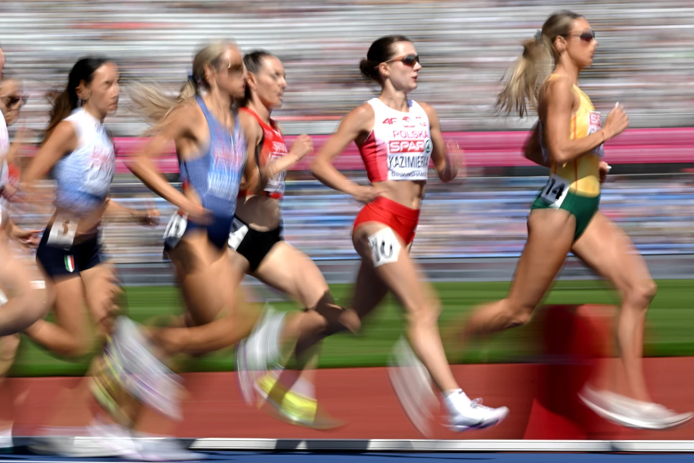 Klaudia Kazimierska na drugiej pozycji Grupa biegaczek w dynamicznym biegu na stadionowej bieżni podczas zawodów lekkoatletycznych, wszystkie skupione i zdeterminowane, w sportowych strojach reprezentujących różne kraje.