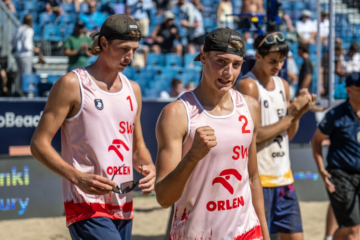 Holting Nilsson i Andersson to wicemistrzowie świata z Adelajdy Dwóch siatkarzy plażowych w biało-czerwonych strojach z logo Orlen, jeden z nich z uniesioną pięścią, wyraża radość po zakończonym meczu, na tle trybun z widownią oraz przeciwników w innych strojach.