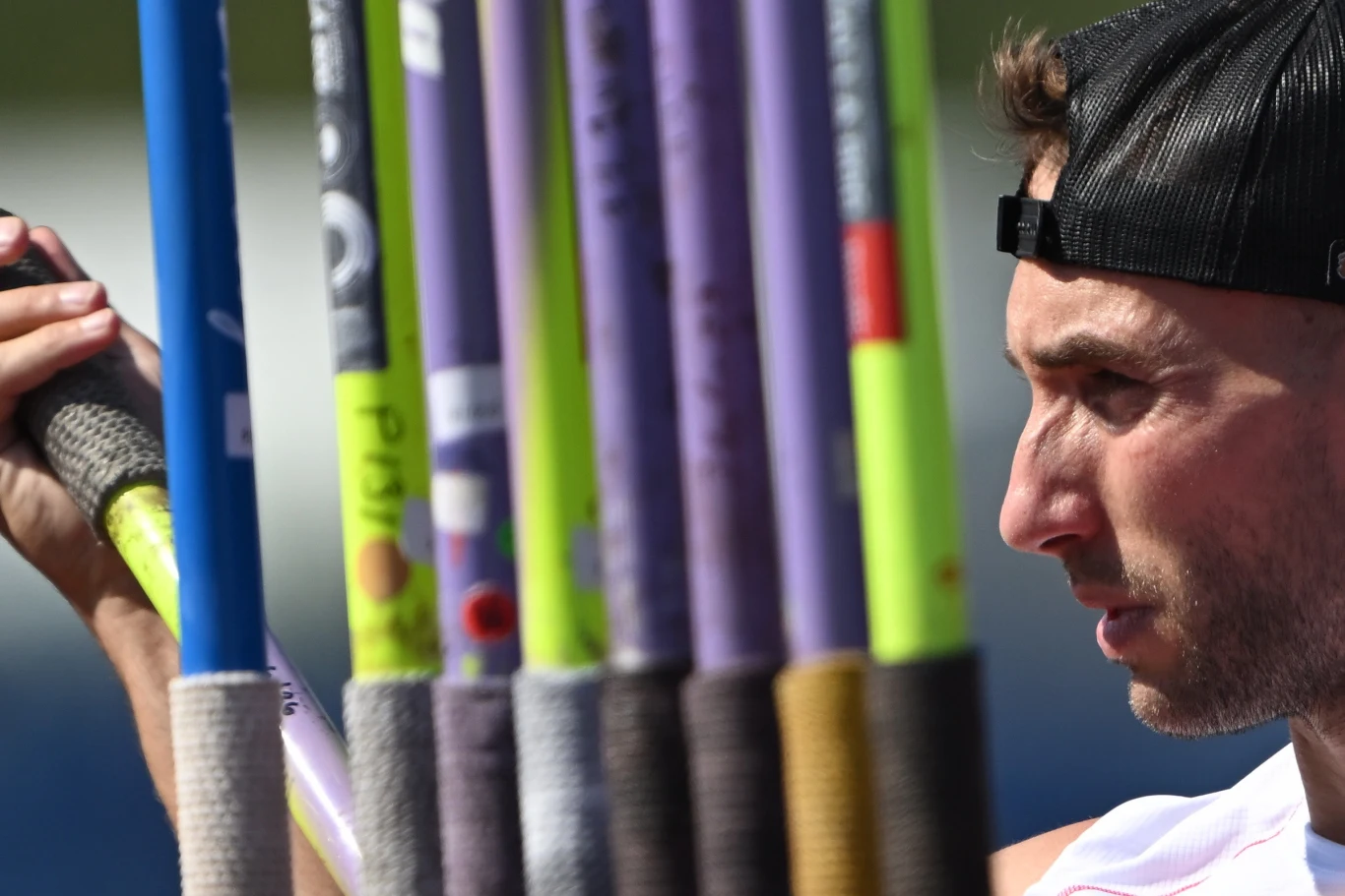 Marcin Krukowski, Birmingham 2026 Sportowiec w czapce z daszkiem wybierający jedną z kilku kolorowych tyczek lekkoatletycznych, skupiony przed konkurencją.