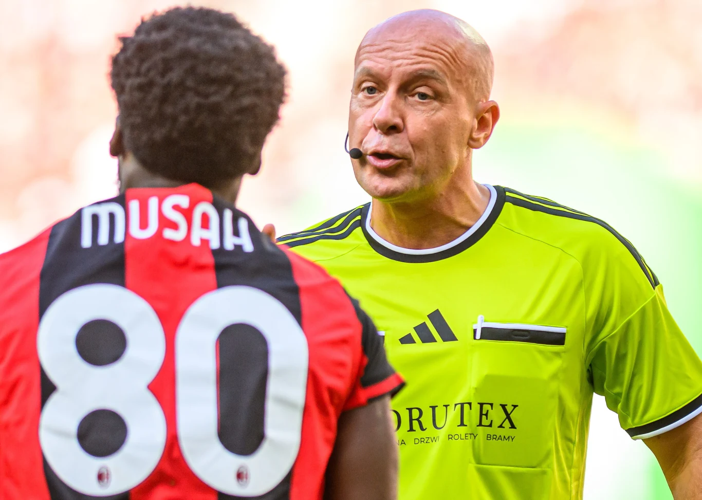 Szymon Marciniak podczas meczu Manchester United - AC Milan Sędzia Szymon Marciniak rozmawia z piłkarzem AC Milan w koszulce z numerem 80 podczas meczu.