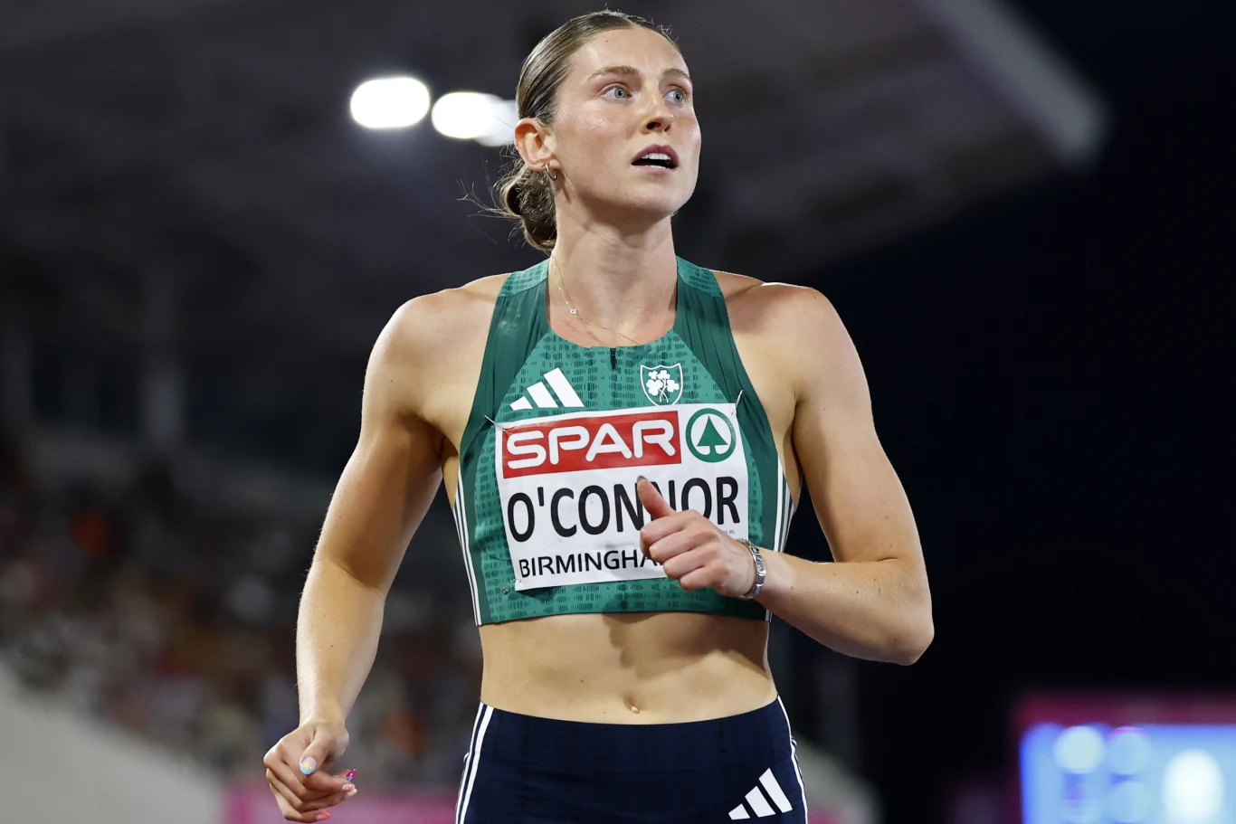 Lekkoatletka w zielonym stroju sportowym z numerem startowym O'Connor podczas zawodów na stadionie, skupiona na trasie biegu.