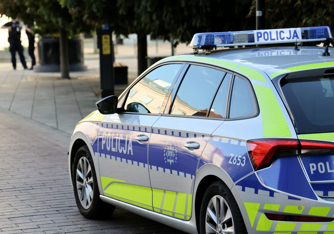 Policja poszukuje sprawcy strzelaniny pod Poznaniem (zdj. ilustracyjne) Radiowóz policyjny z niebiesko-żółtymi pasami i napisem 'Policja' zaparkowany przy chodniku w mieście.