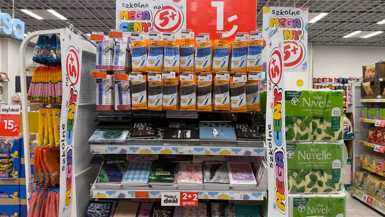 Długopisy BIC za 6 zł w Dealz. Są też wymazywalne Regał w sklepie z artykułami szkolnymi, na którym znajdują się długopisy, zeszyty oraz notatniki rozmieszczone w rzędach, a nad nimi widoczna jest informacja o promocyjnej cenie 1 zł.