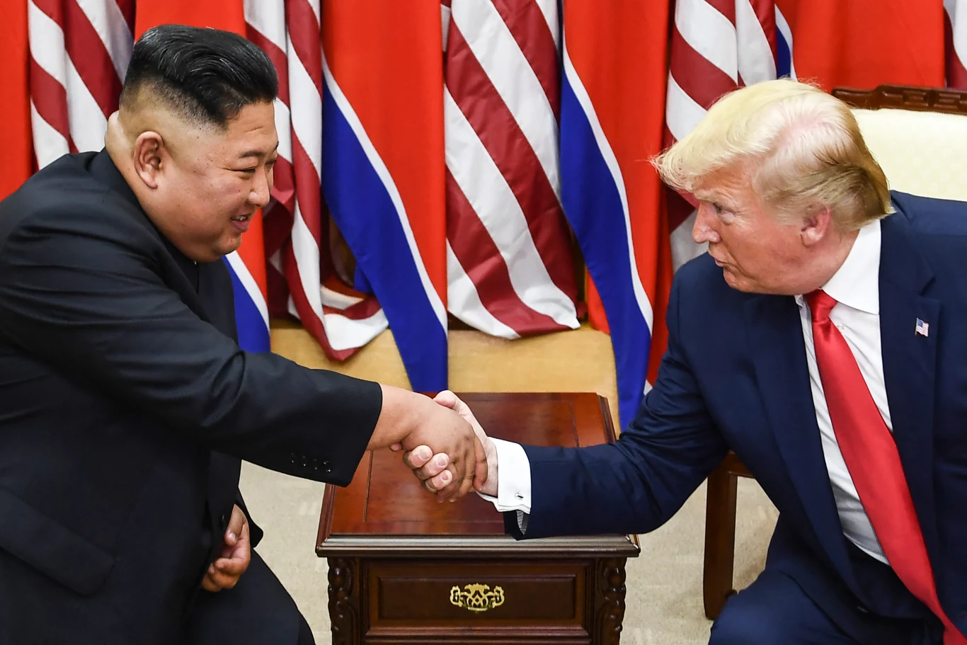 Donald Trump planuje jesienią 2026 spotkanie z Kim Dzong Unem podczas szczytu APEC. Kim Dzong Un i Donald Trump ściskają sobie dłonie, siedząc naprzeciwko siebie przy niewielkim stoliku, w tle widoczne flagi.