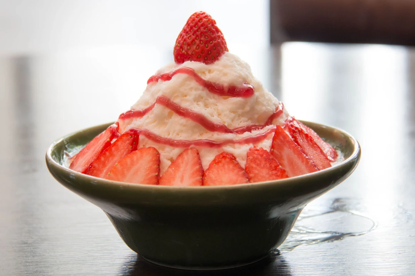 Owocowy i puszysty deser lodowy. Nie ma nic lepszego na upały Porcja bingsu udekorowana plasterkami truskawek, polana syropem truskawkowym, z połówką truskawki na wierzchu.