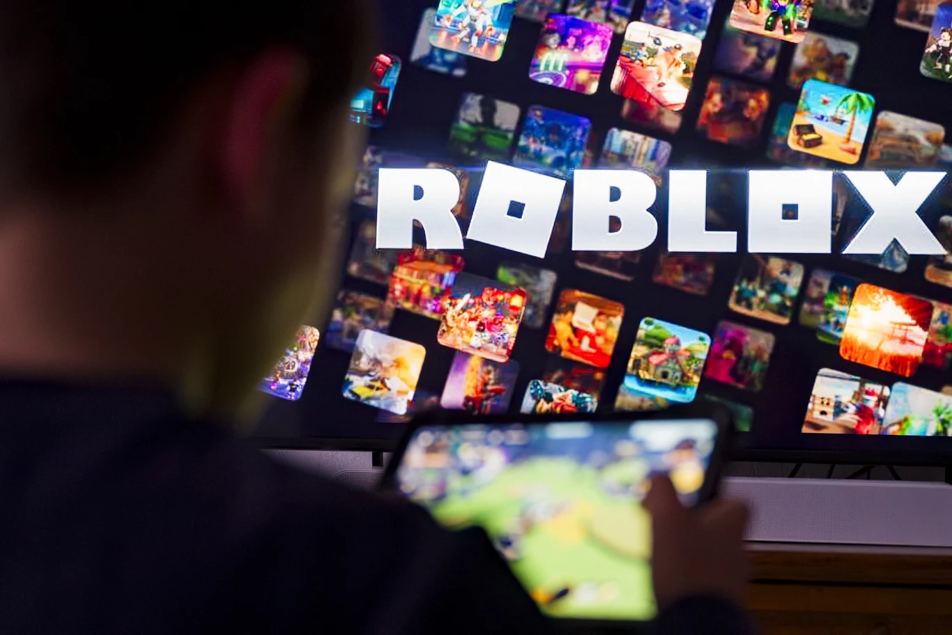 Senat USA wziął pod lupę grę Roblox Osoba grająca na tablecie przy ekranie z logo Roblox otoczonym miniaturami różnych gier.