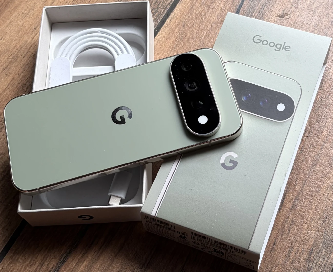 Zawartość opakowania z Google Pixel 11 Pro. Nowoczesny smartfon Google w jasnozielonym kolorze z dużym modułem aparatu, kabel ładowania oraz oryginalne opakowanie z widocznym logo firmy.