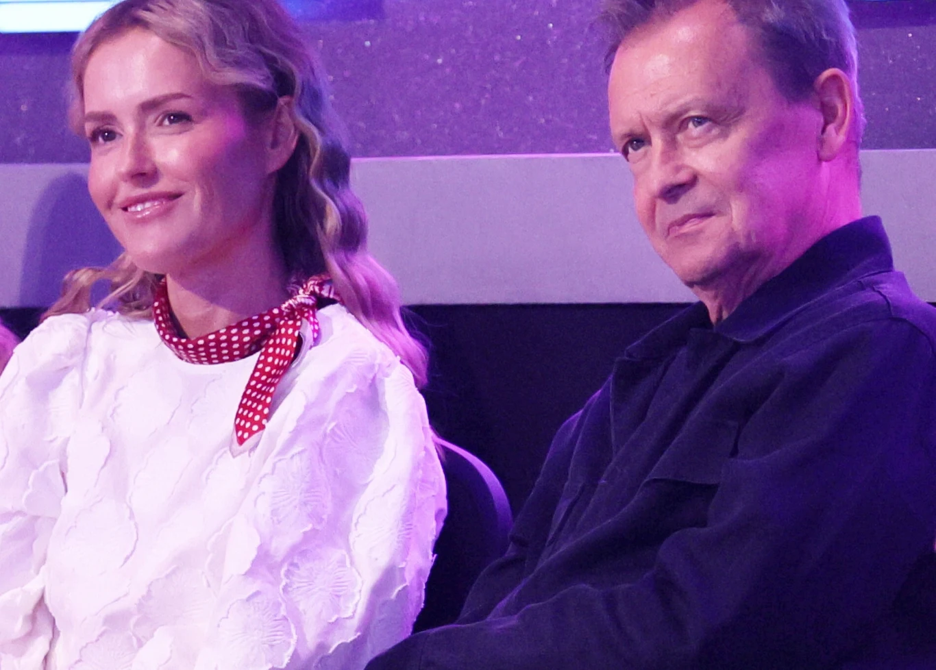 Olga Frycz, Jan Frycz Dwie osoby siedzące obok siebie, kobieta w jasnej bluzce z czerwonym szalikiem oraz mężczyzna w ciemnej koszuli, skierowani lekko w stronę rozmówcy, w tle fioletowe światło.