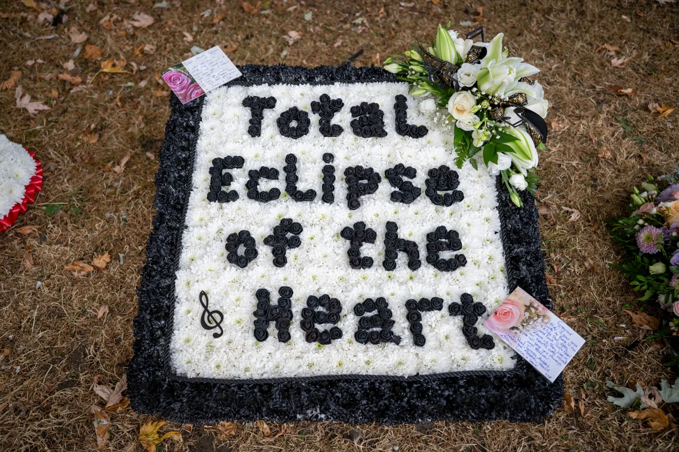 Kwiatowa kompozycja w kształcie kwadratu z napisem 'Total Eclipse of the Heart', ozdobiona nutką oraz bukietem białych kwiatów w prawym górnym rogu i dwoma kartkami z wiadomościami.