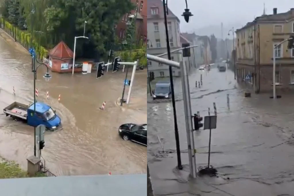 Skutki ulew w Głuchołazach Zalana ulica w Głuchołazach, samochody przejeżdżające przez wodę, częściowo zanurzone znaki drogowe, deszczowa aura