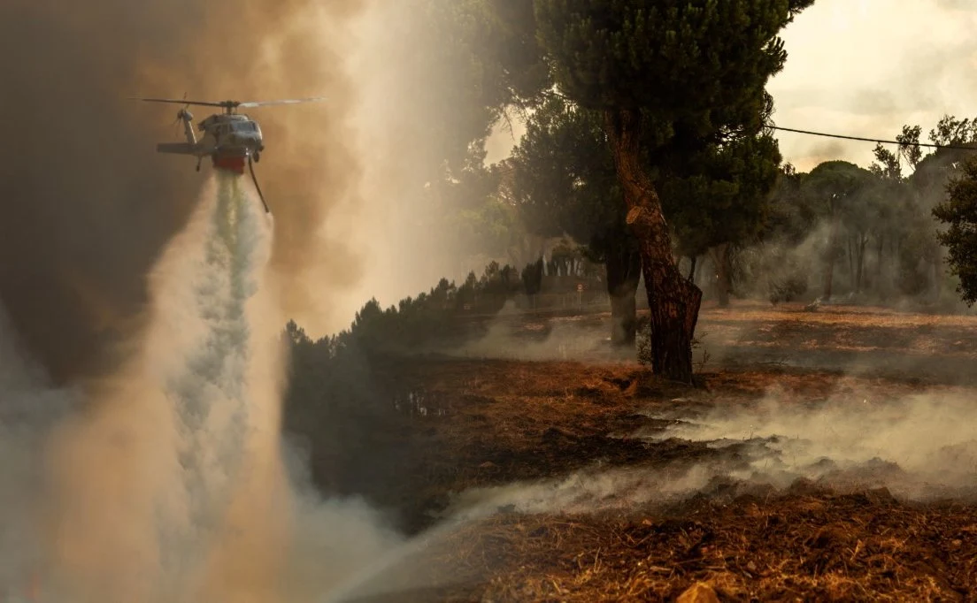 Hiszpania walczy z suszą. Tymczasem Portugalie trawią pożary lasów i łąk Helikopter zrzucający wodę na płonący las, gęsty dym i zwęglona ziemia wokół ogniska pożaru w Portugalii.