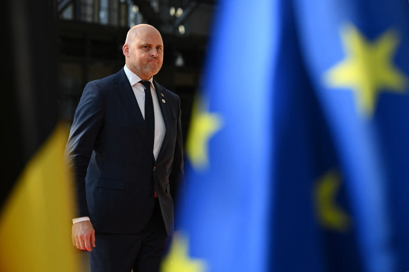 Premier Łotwy Andris Kulbergs żąda od Brukseli miliardów euro Andris Kulbergs w garniturze stoi obok flag Unii Europejskiej i Belgii podczas spotkania w Brukseli.