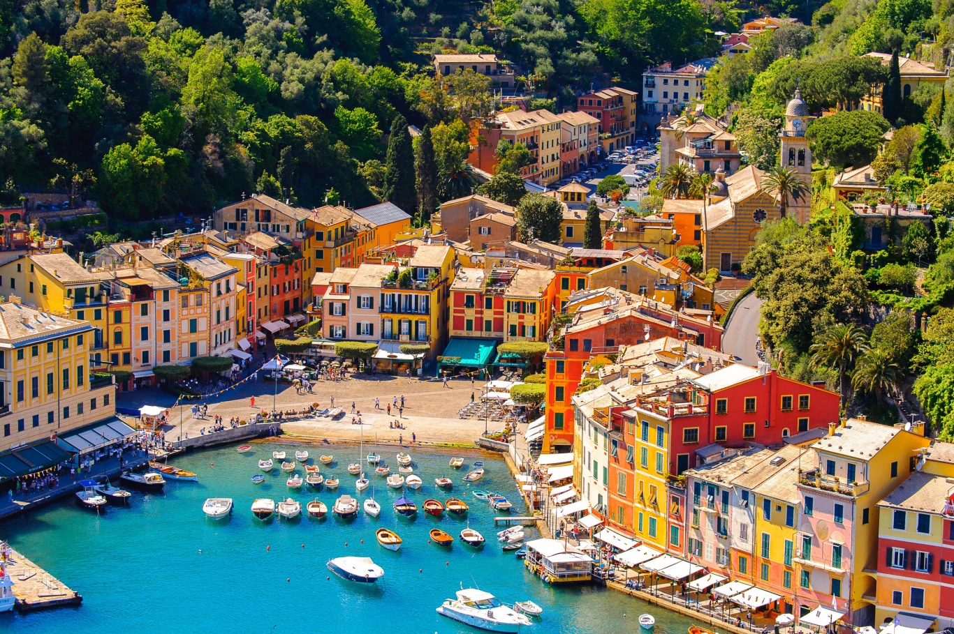 Portofino Malownicze, kolorowe kamienice otaczające niewielki port z zacumowanymi łodziami, w otoczeniu bujnej zieleni nad wybrzeżem.